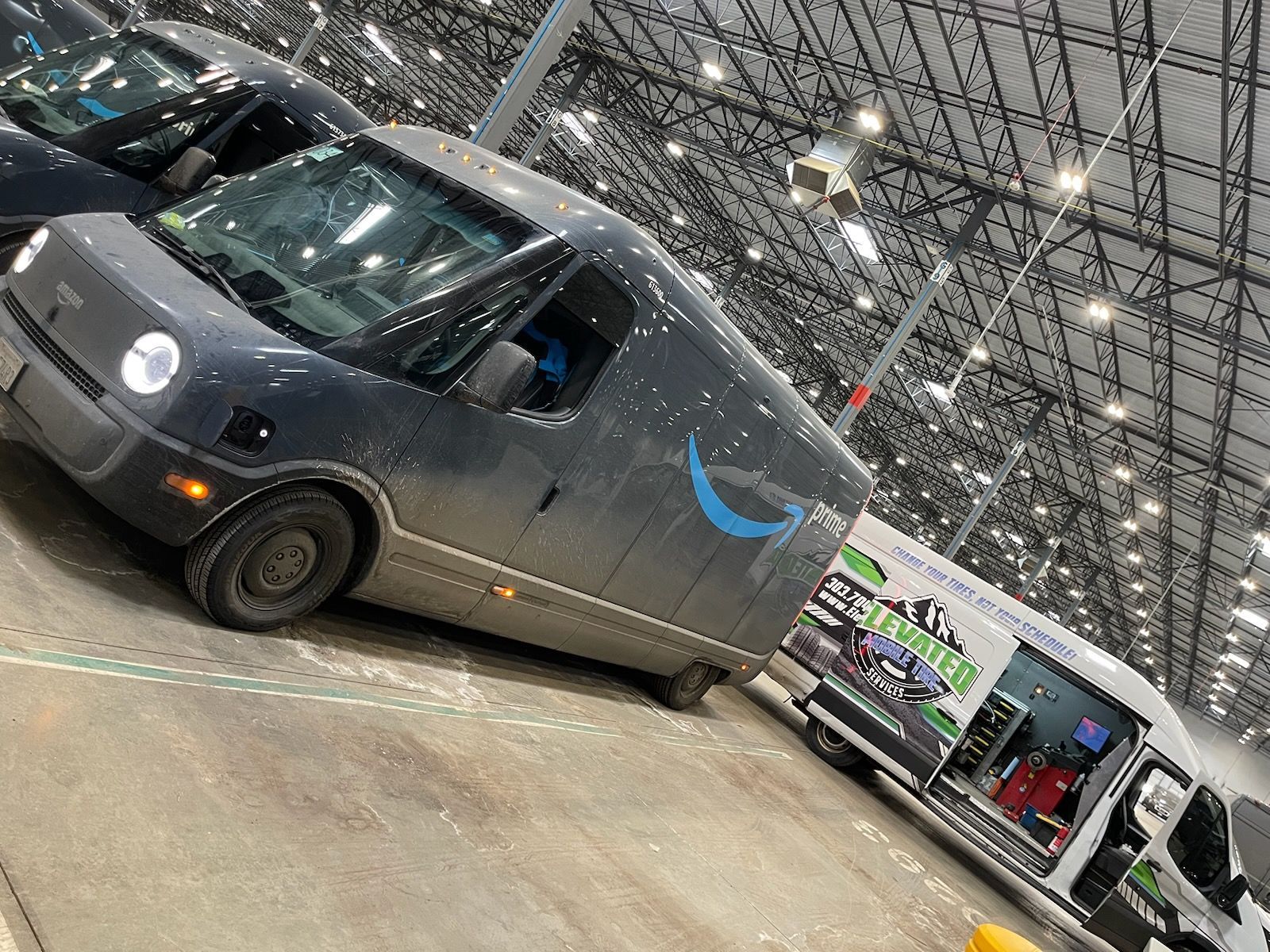 An Amazon delivery van parked in a warehouse next to a truck.