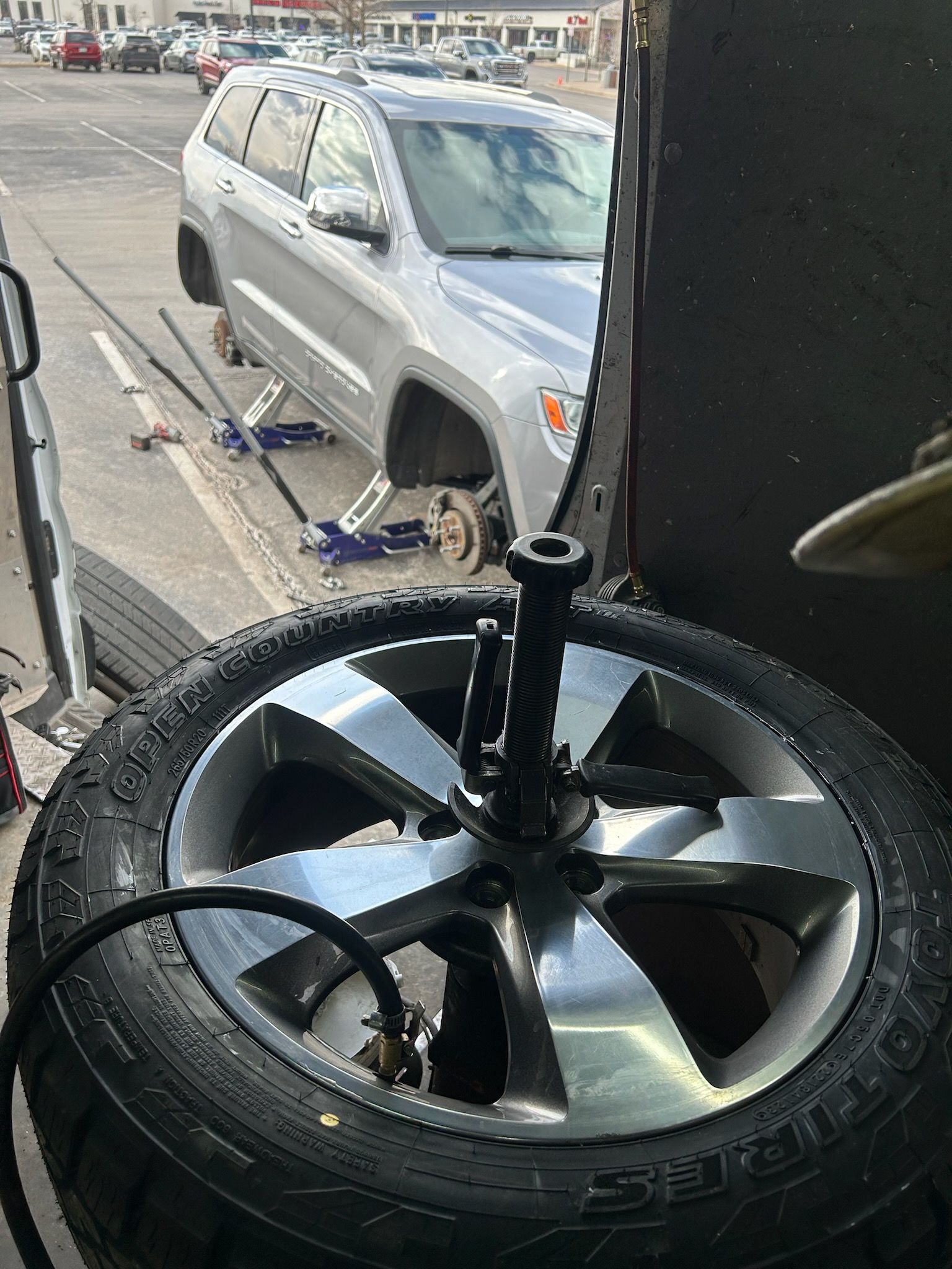 A silver SUV with wheels removed, being worked on outside, tire machine in foreground.