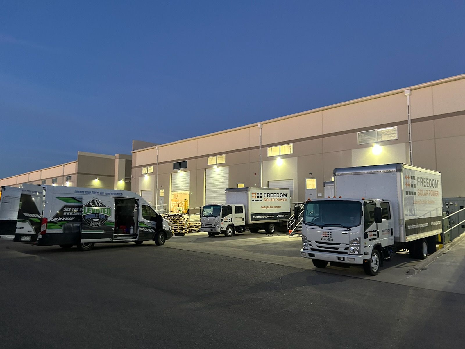Vehicles parked outside a large warehouse loading dock at dusk.