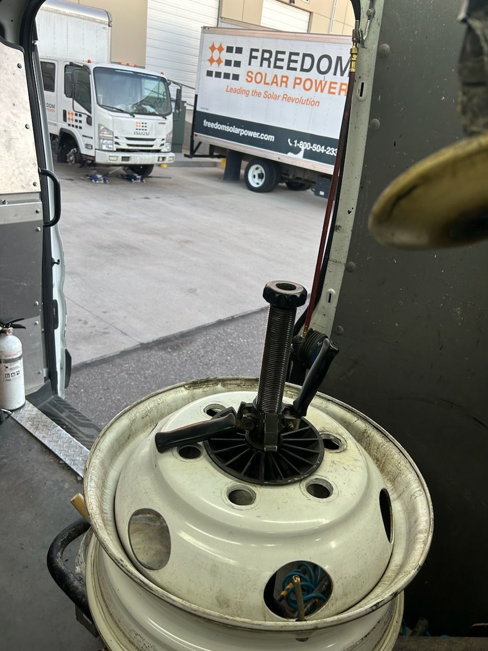 Inside a truck, tire with a tool on top, looking out at two trucks in a parking lot.