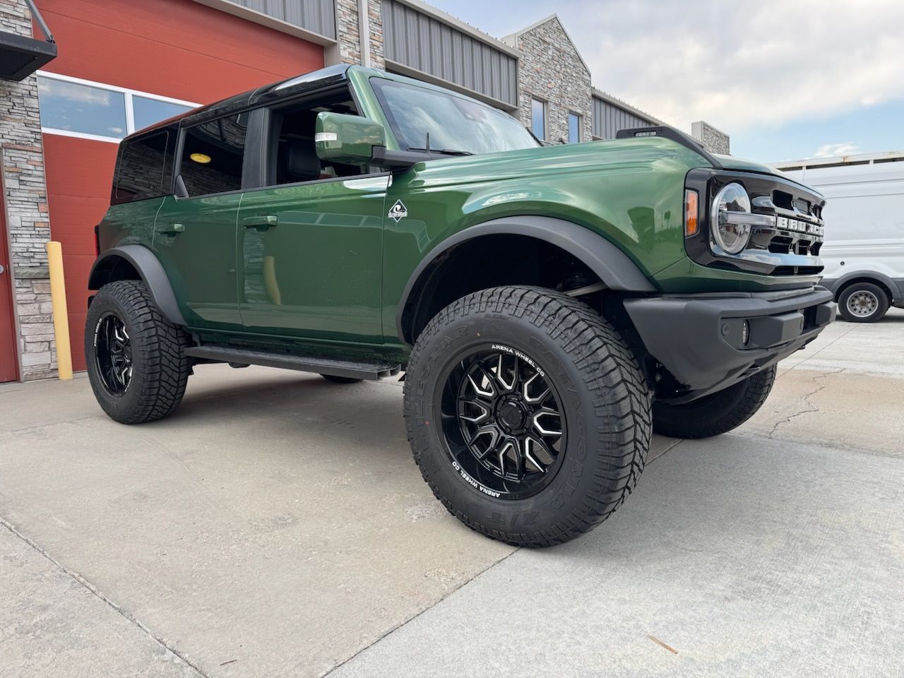 Green Ford Bronco SUV with black wheels parked outside.