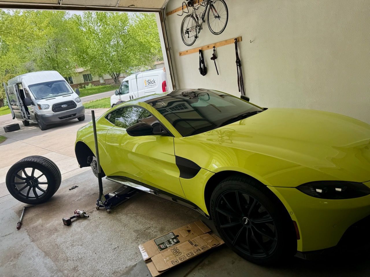 Yellow sports car being repaired in a garage, with tools, a tire, and service vans visible.