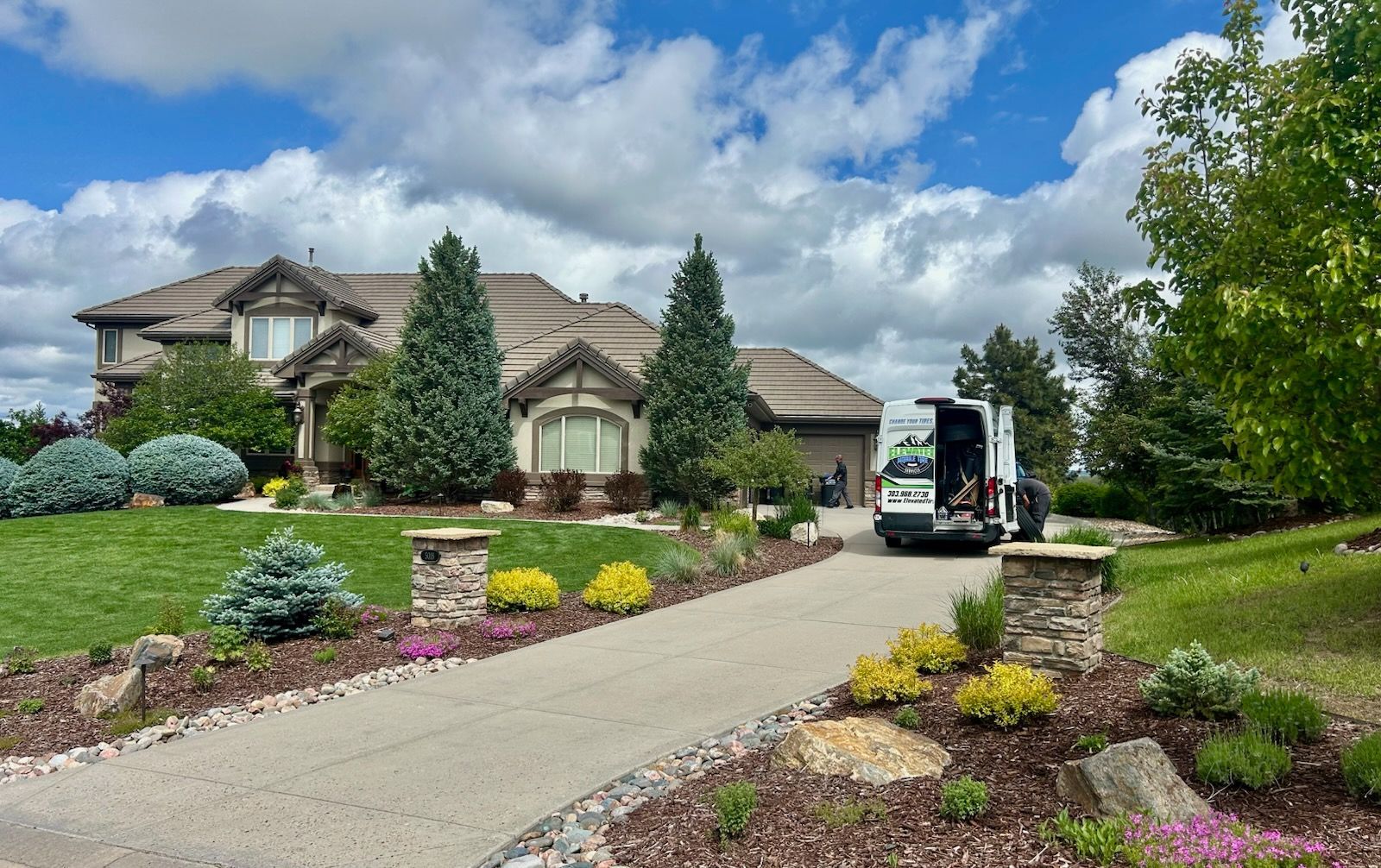House with manicured lawn, truck in driveway, under blue sky with clouds.