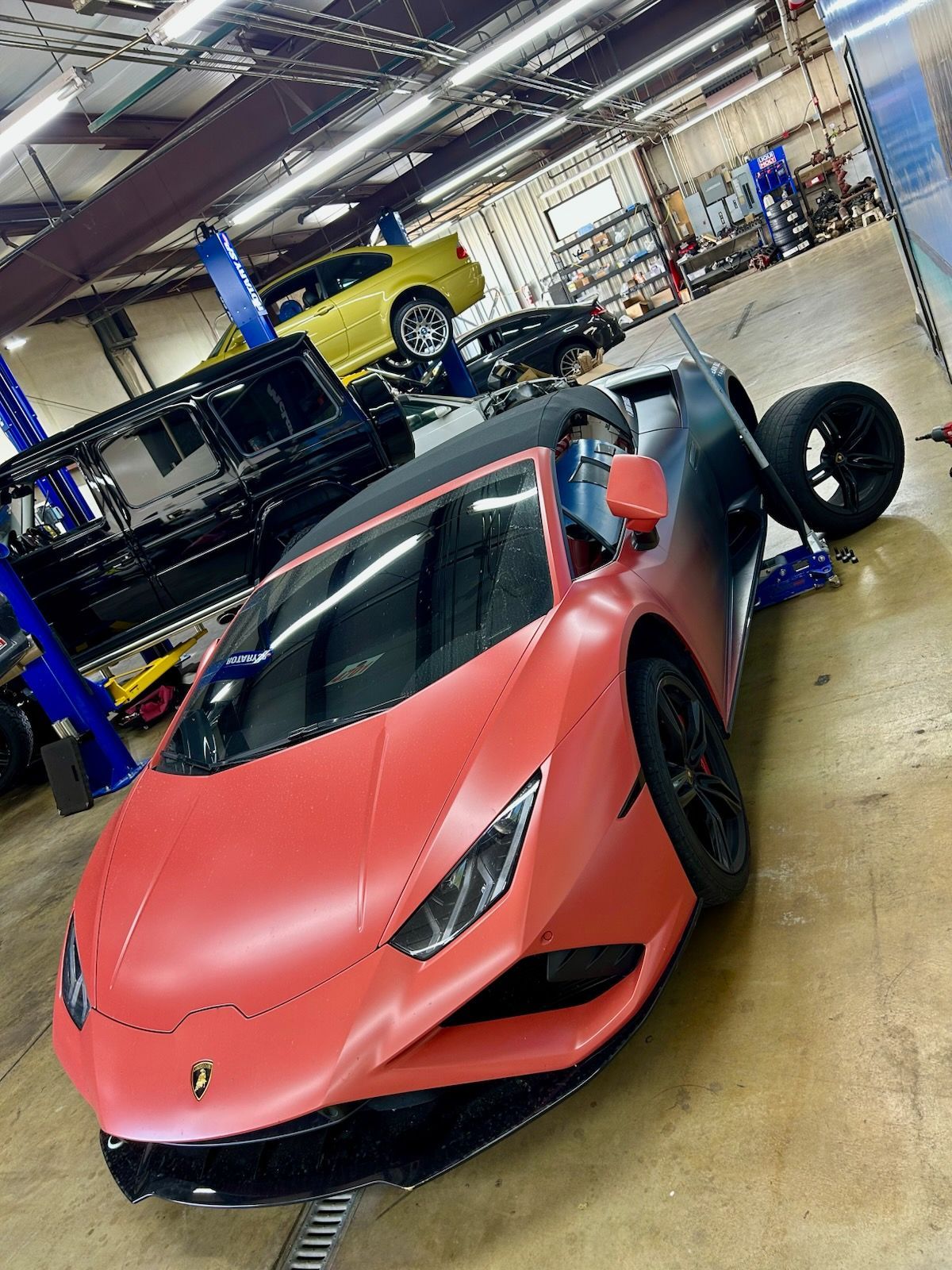 Lamborghini in a garage, red and black paint, being worked on. Other cars on lifts.