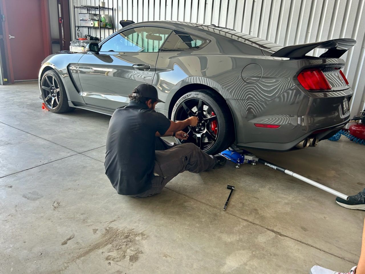 Man changing tire on a gray sports car in a garage.