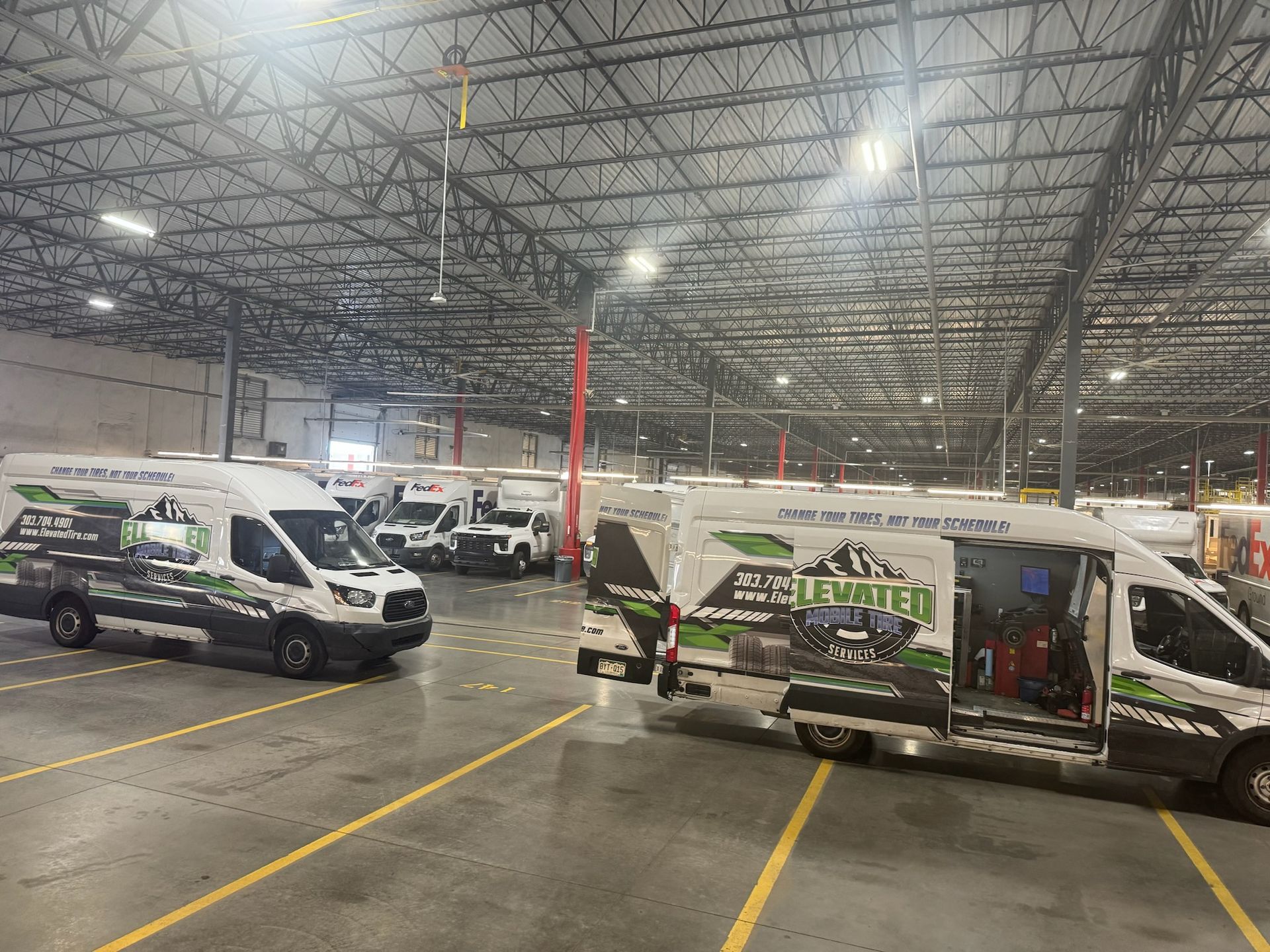 Fleet of white service vans with green logos parked inside a large warehouse.