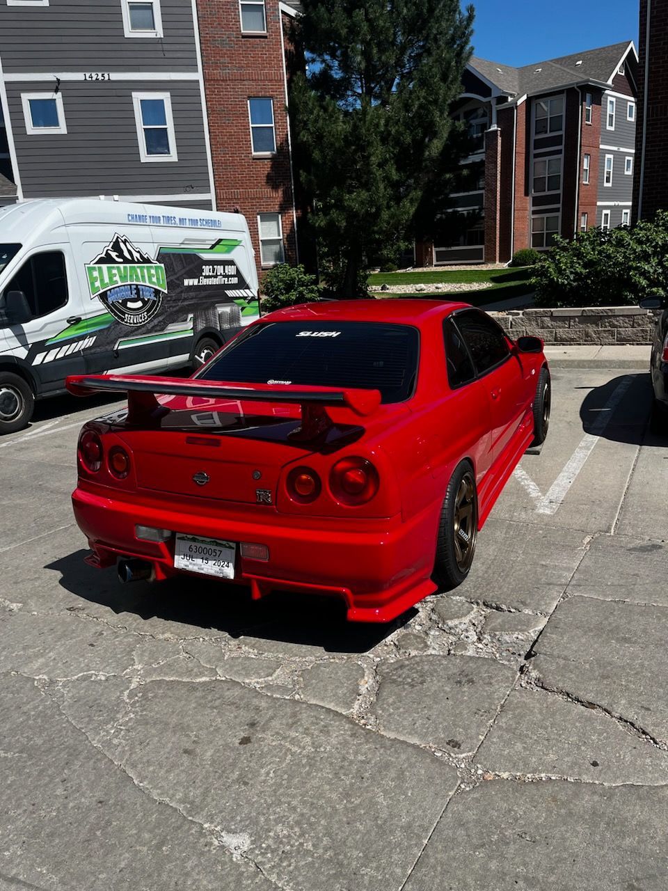 Red Nissan Skyline R34 sports car parked in a parking lot on a sunny day.
