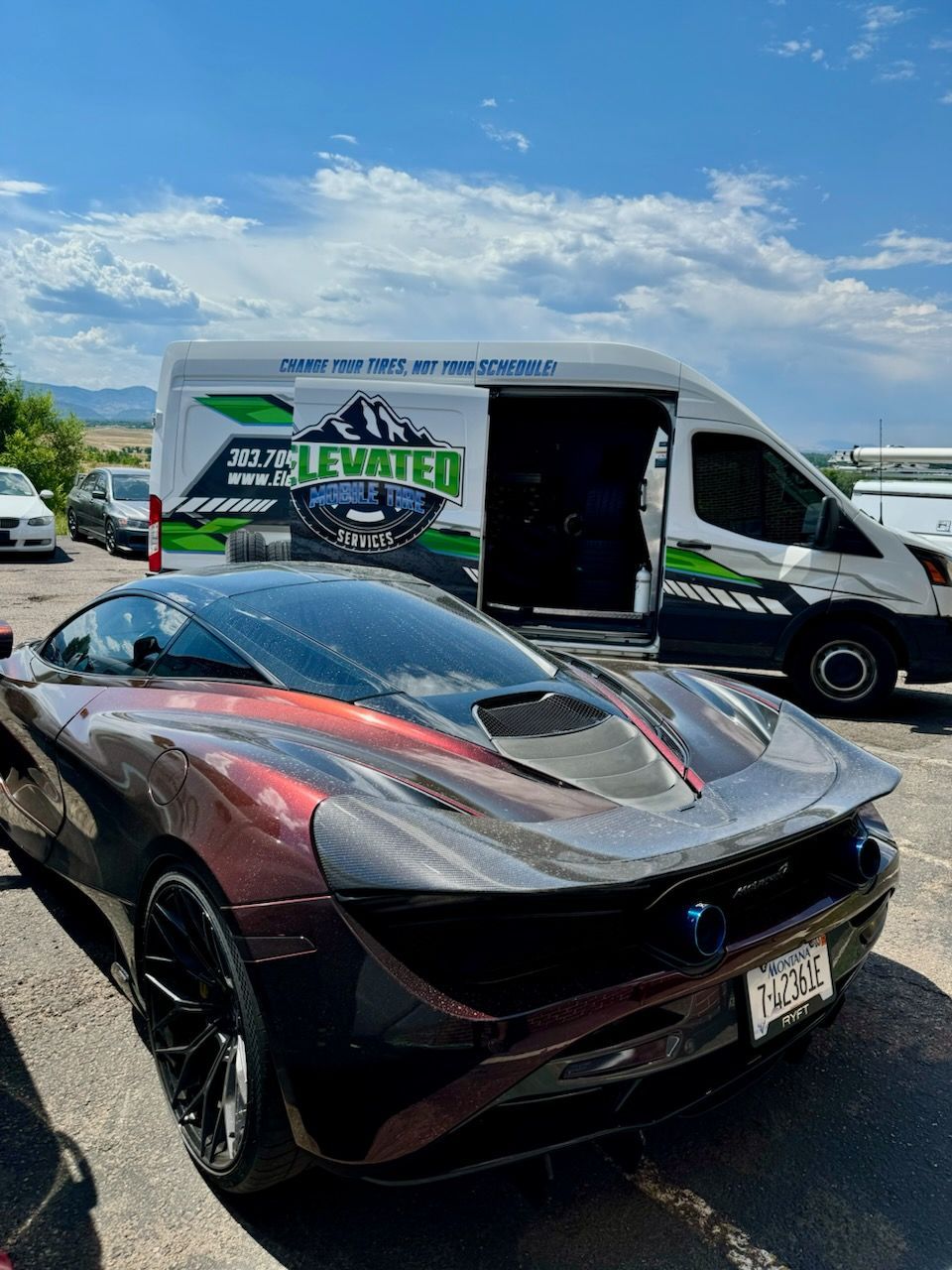 McLaren sports car with color-shifting paint in front of a service van under a blue sky.