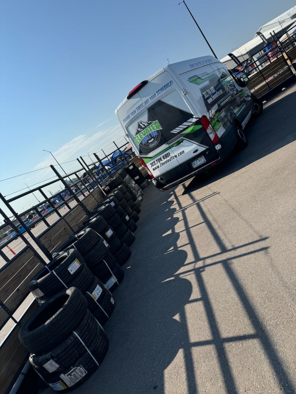 Van with logo parked near tires and fence, sunny day.