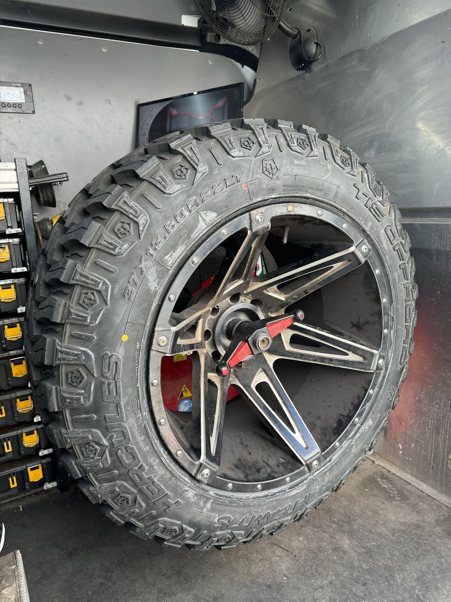 Spare tire and rim in a vehicle; tire is black and rim is black with silver accents.