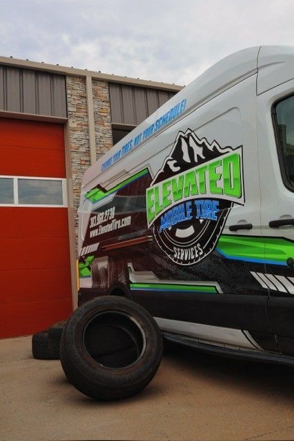 Elevated Mobile Tire Services van with tire, parked in front of a red door. Logo features a mountain.