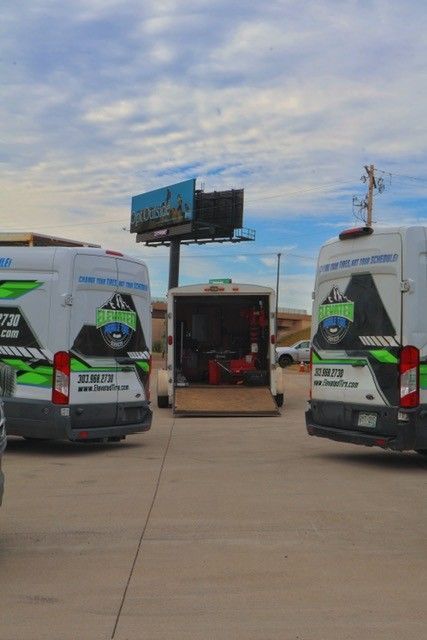 Three landscaping trucks parked in lot, with a trailer and billboard overhead.