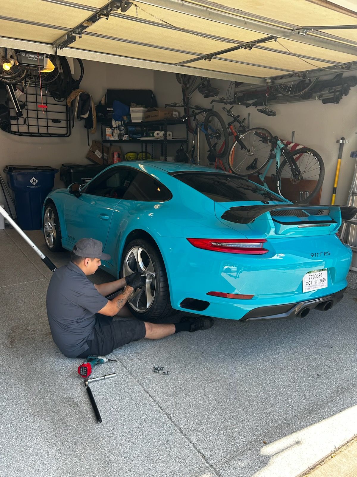 Man changing a tire on a turquoise Porsche in a garage.