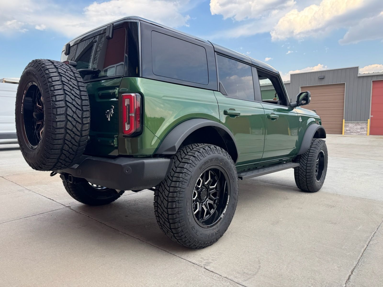 Green Ford Bronco SUV with black wheels, spare tire, and tinted windows. Parked outdoors.