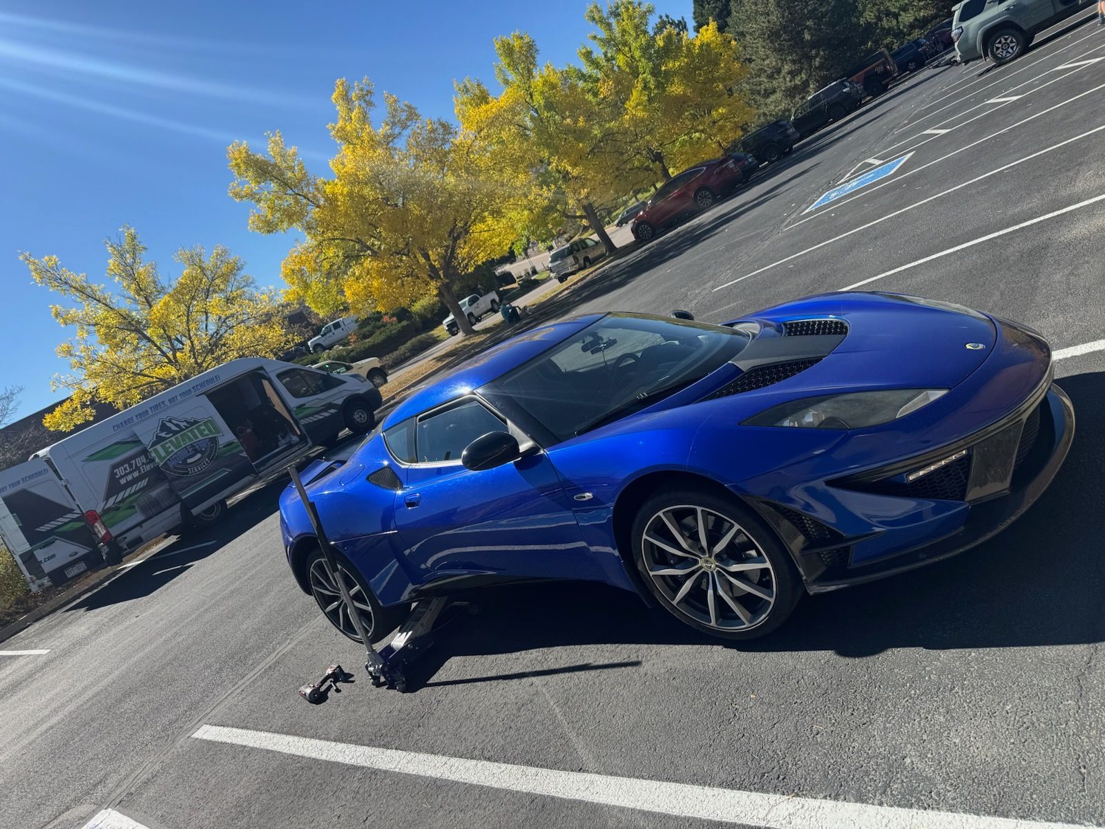 Blue Lotus sports car parked in a parking lot, with a trailer visible in the background.