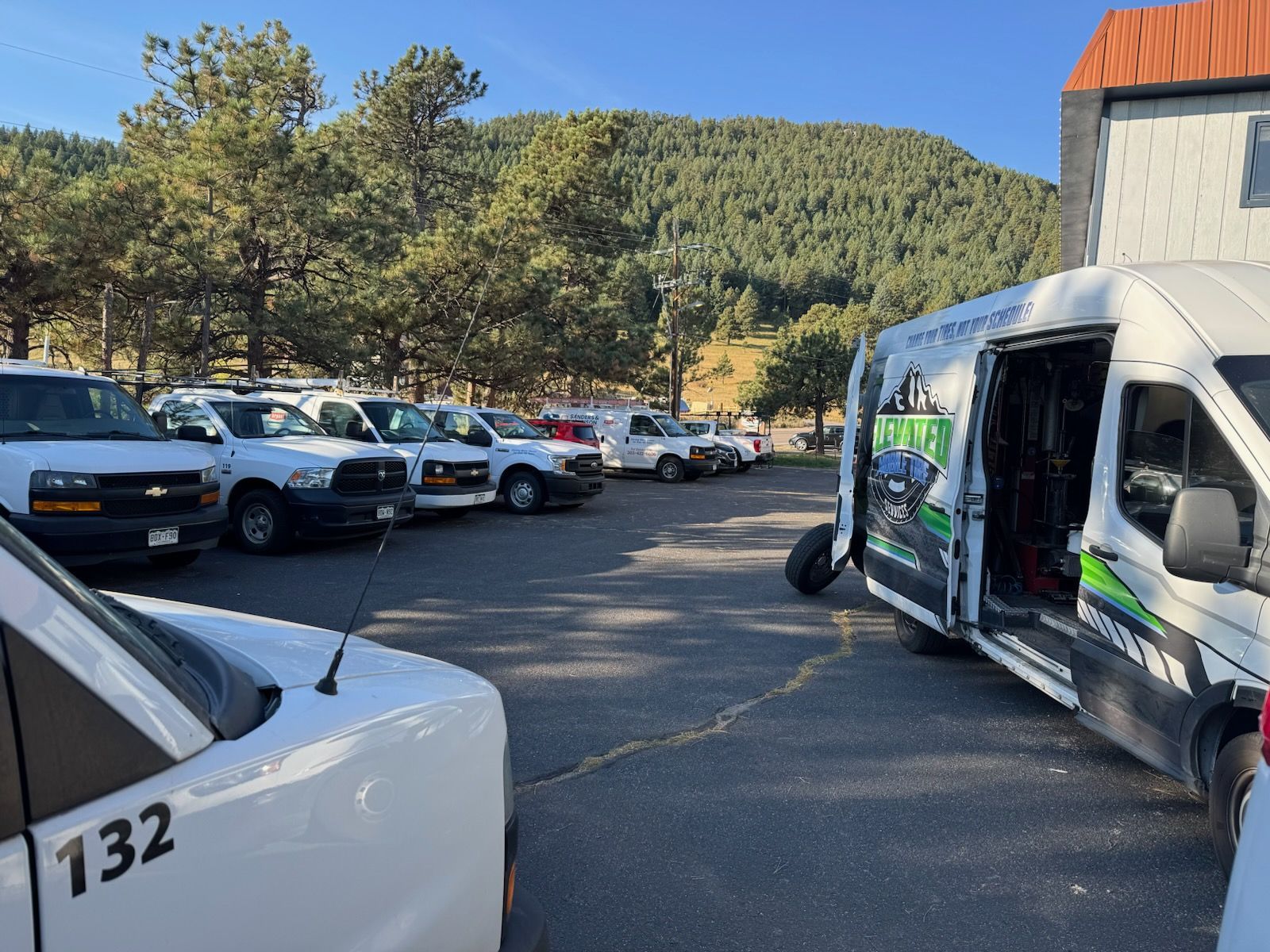 A parking lot with white work vans. A mountain and blue sky are in the background.