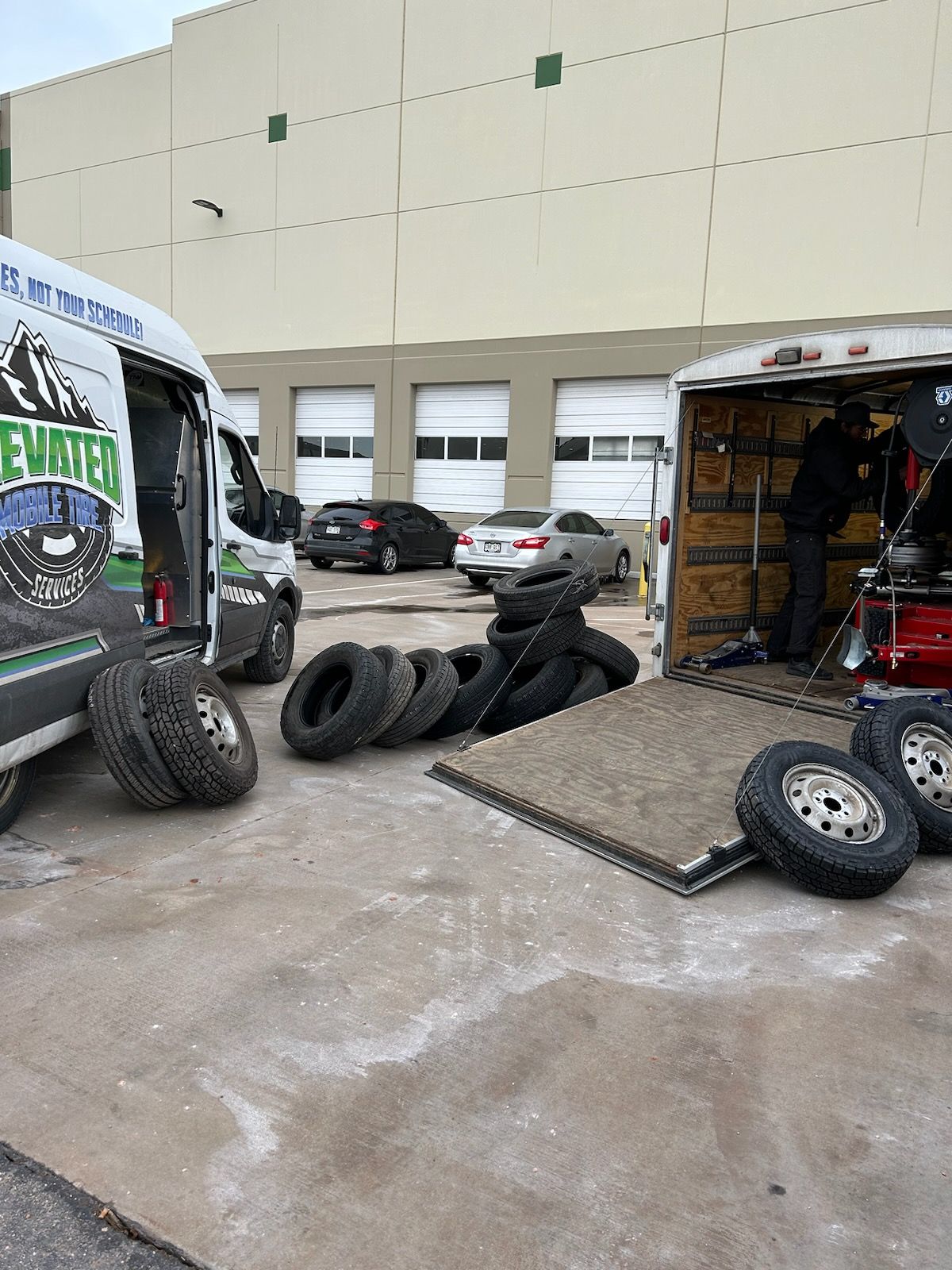 A tire service setup outdoors: a van, a trailer with a person, tires on ground.