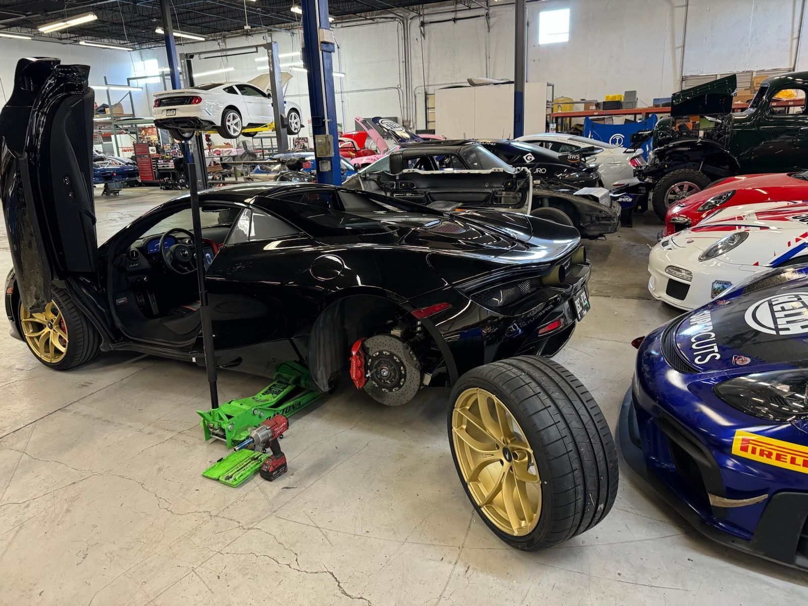 Black sports car with open door and gold wheels being worked on in a garage.