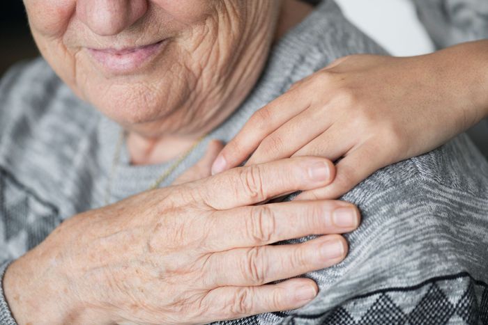 Elderly woman's hands clasped by another's hand. Gray sweater, wrinkled skin, showing comfort and support.