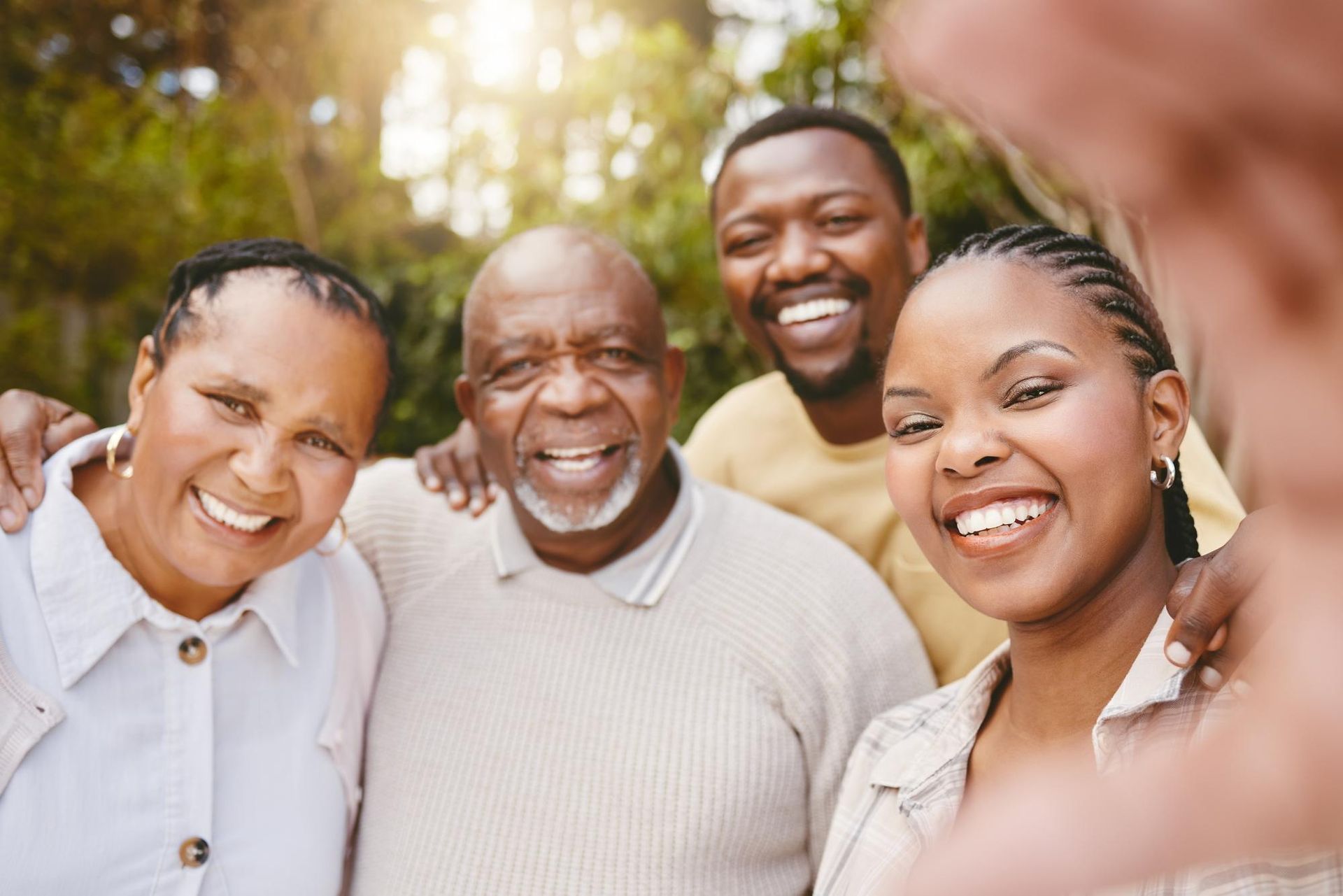 Family of four smiling at the camera, outdoors; warm sunlight.