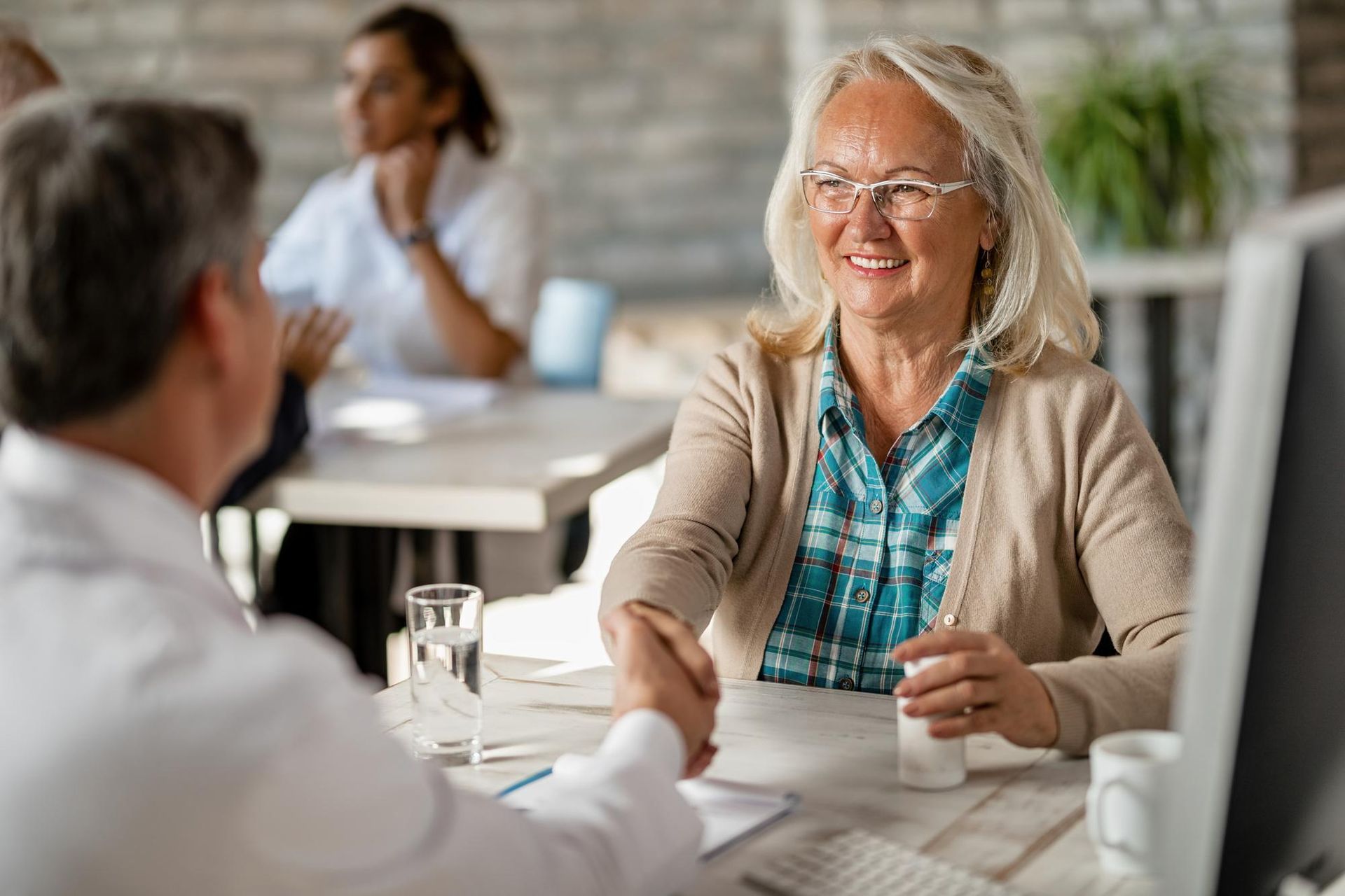 Senior woman shaking hands with doctor, smiling; office setting.