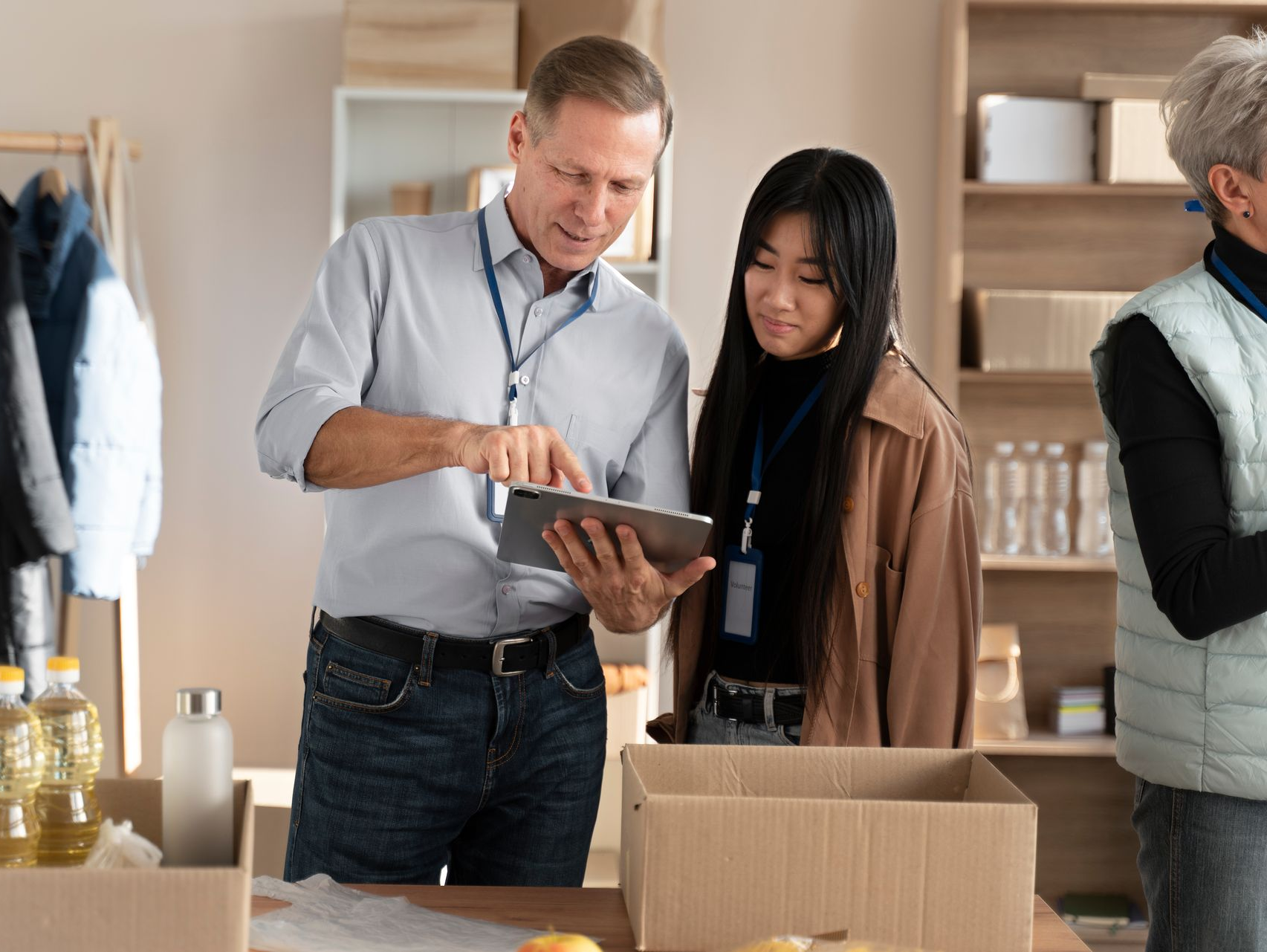 Man and woman looking at a tablet in a store, boxes and shelves in the background, other people present.