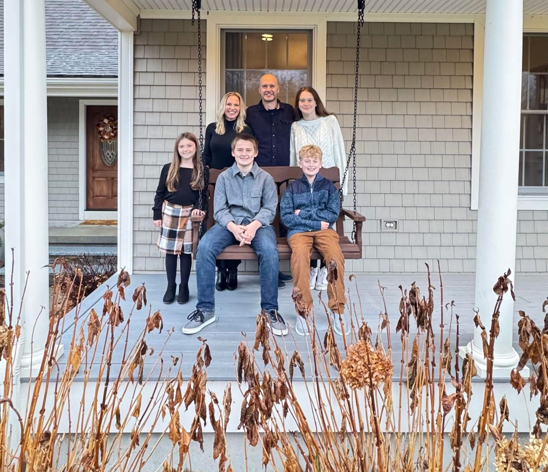 Family of seven poses on a porch swing in front of a house.