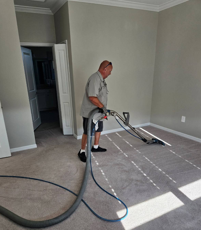 Worker vacuuming carpet in a sunlit room with a large hose and cleaning machine