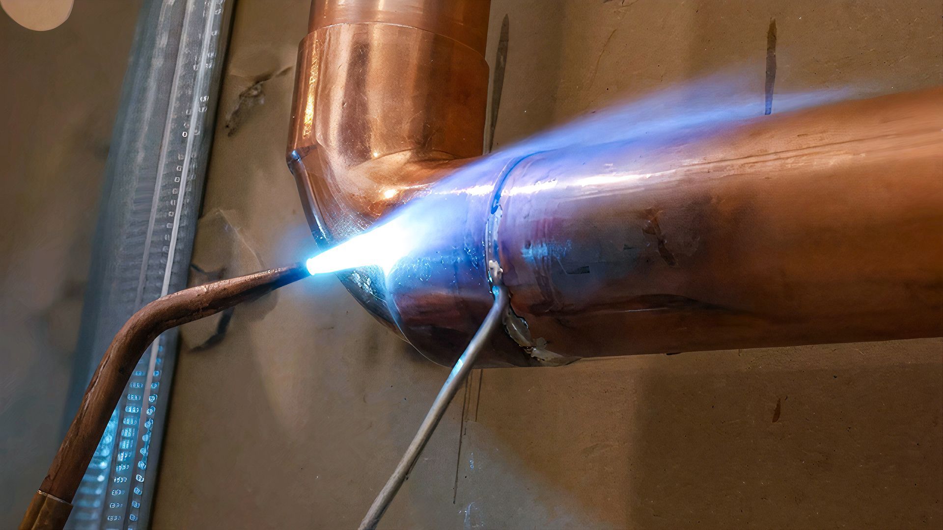 Torch welding a copper pipe joint, with bright blue flame and sparks in a workshop setting