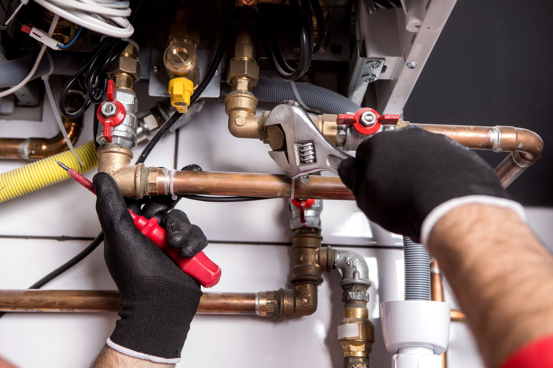 Gloved hands using wrenches to repair copper plumbing pipes under a sink