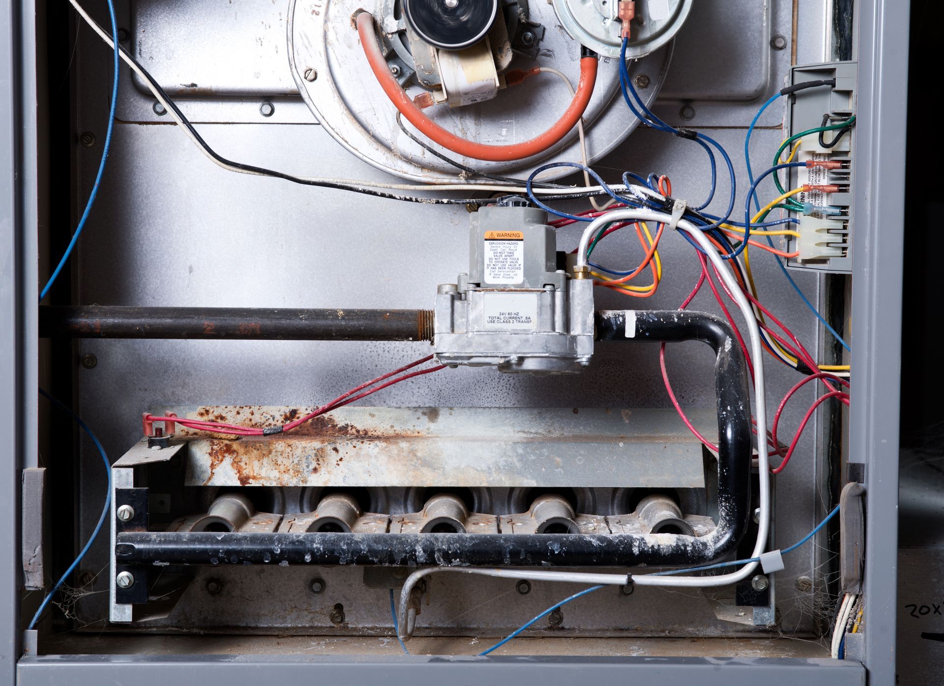 Open furnace cabinet with exposed wires, blower, and gas burners inside a metal unit