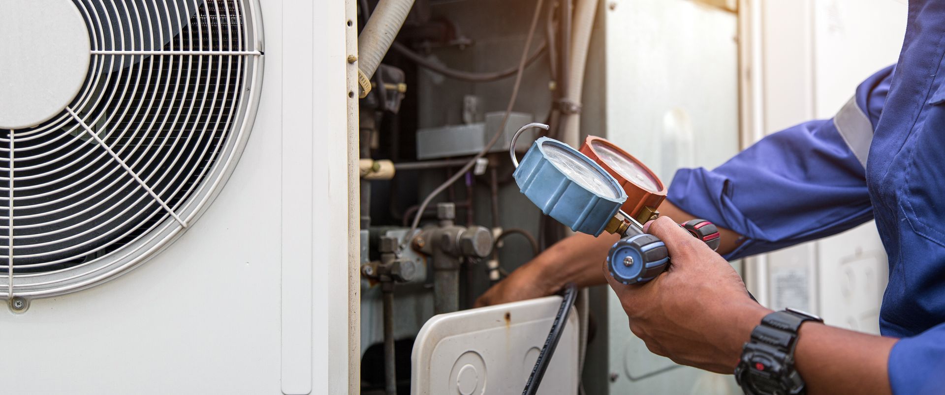 Technician checking HVAC unit with pressure gauge and wires outside a building