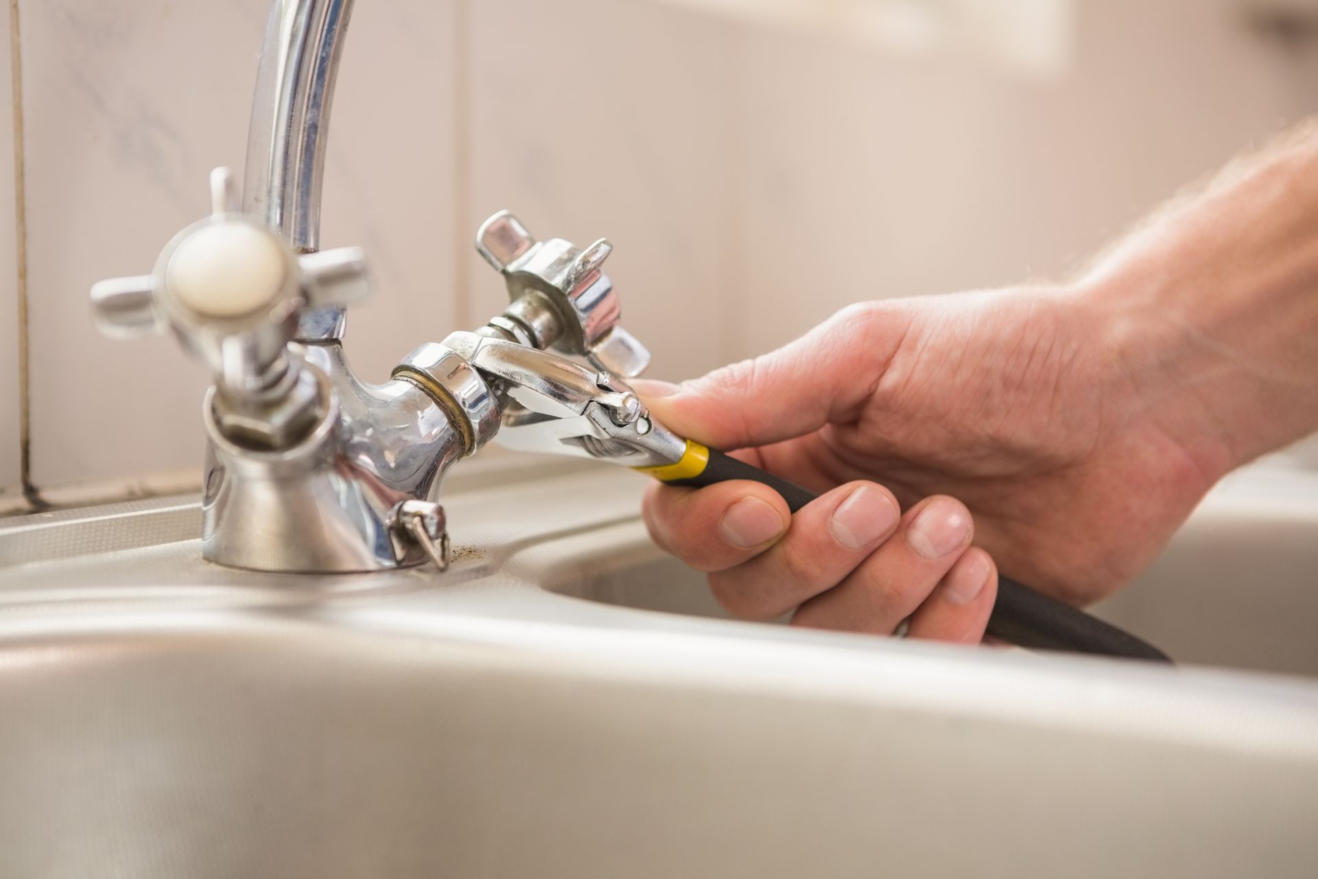 Hand repairing a chrome bathroom faucet with a wrench beside a sink