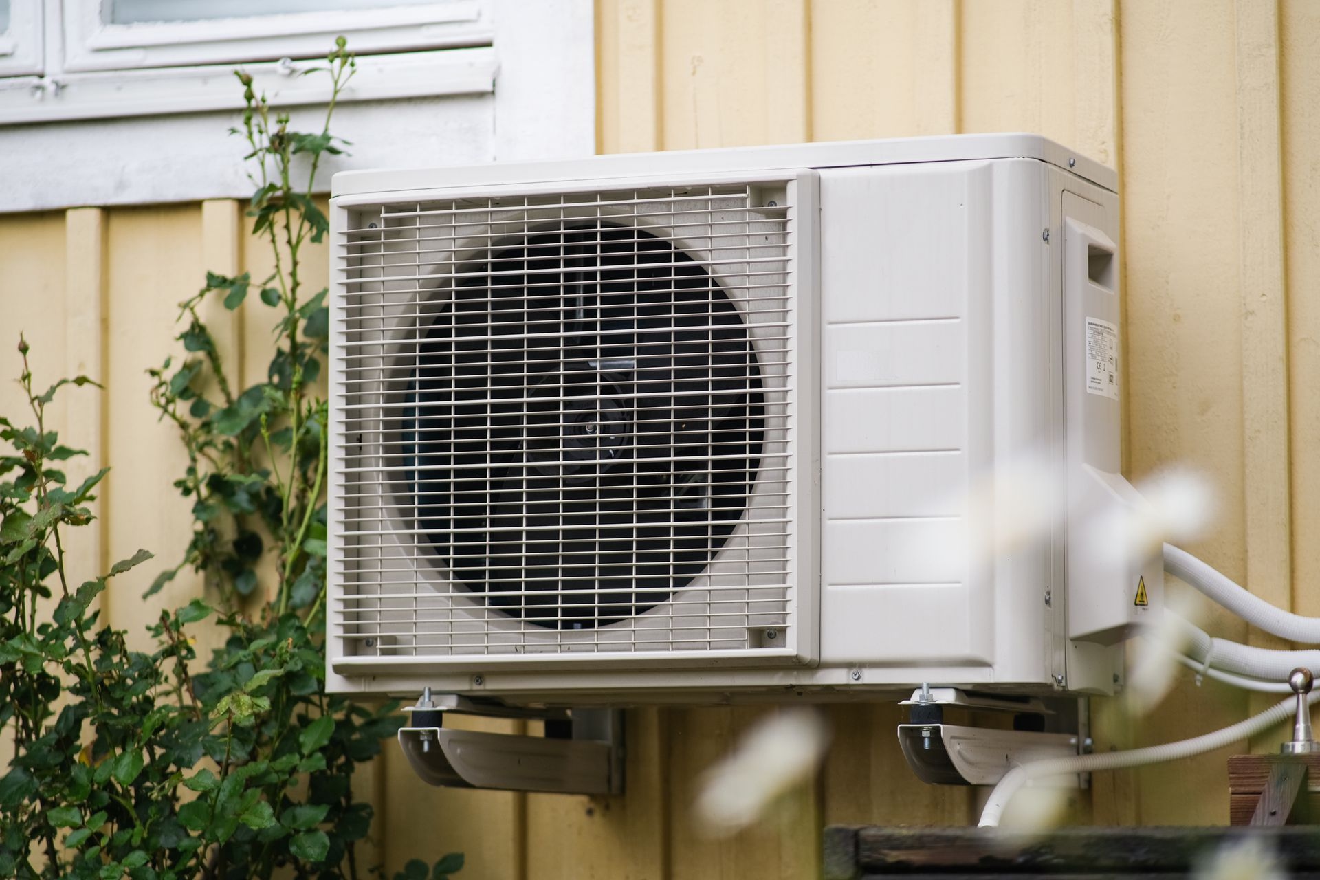 Outdoor air conditioning unit mounted on a wall beside a building with hoses attached