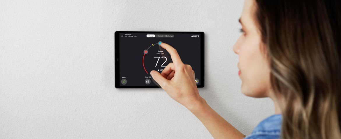 Person adjusting a wall-mounted Lennox smart thermostat displaying 72° in a home interior
