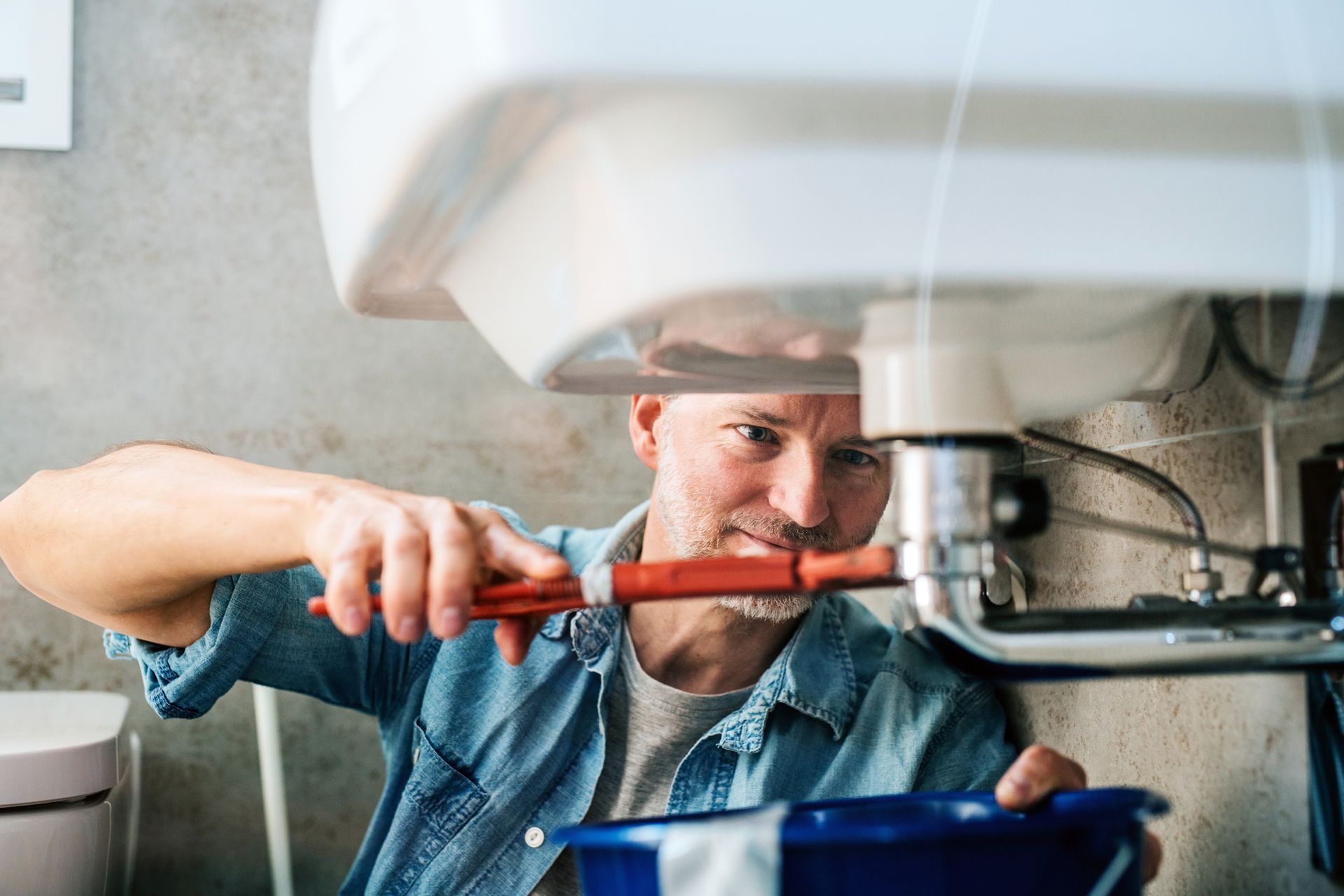 Plumber tightening a faucet under a sink with a red wrench