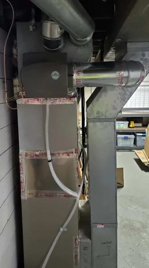 Industrial ductwork and insulation in a mechanical room, with exposed pipes and metal supports.