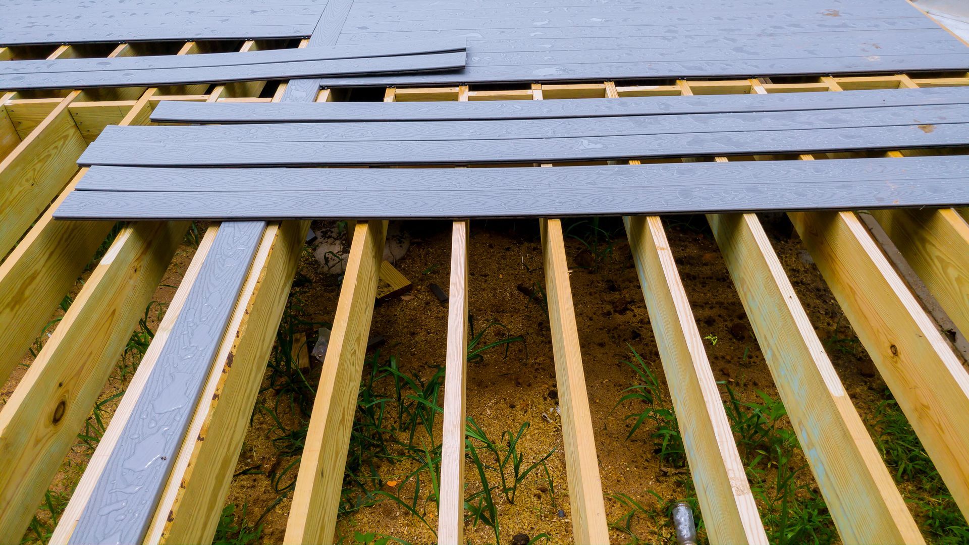 Wooden deck frame with grey planks partially laid. Construction in progress.