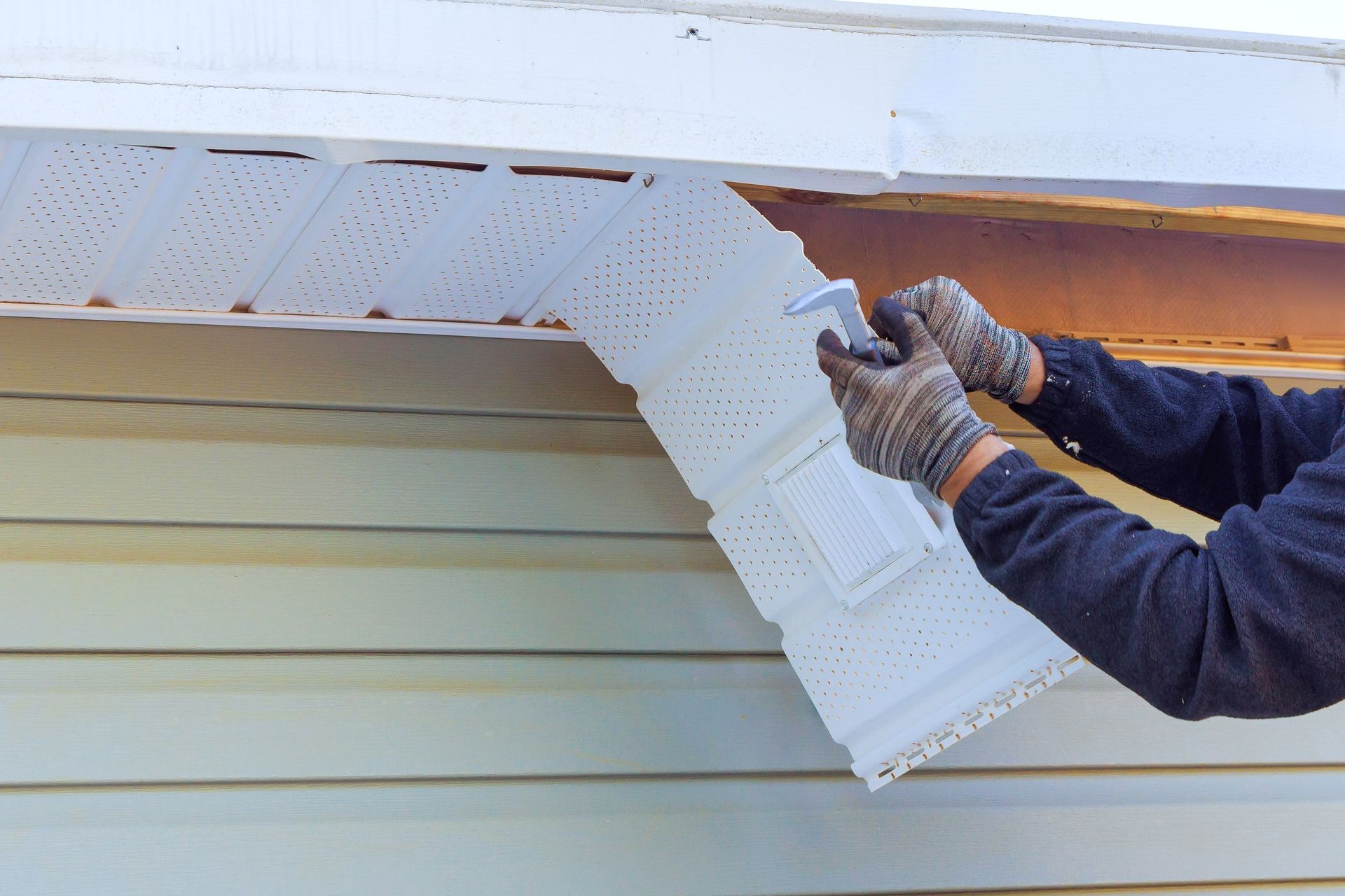 Person in gloves removing white vinyl siding from a house.