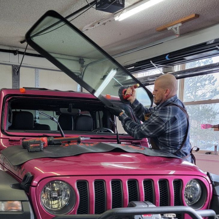 A man is working on the windshield of a pink jeep