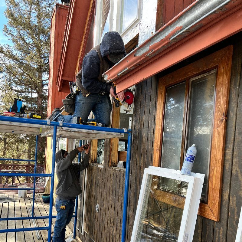 A man is standing on a scaffolding fixing a window on a house.