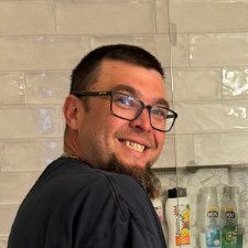 A man with glasses and a beard is smiling in a bathroom.