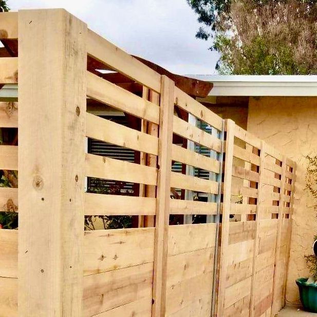 Wooden slatted fence alongside a light-colored building, outdoors.