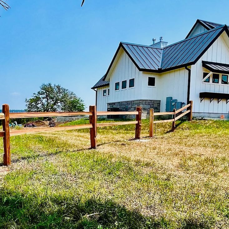 Wooden fence in a grassy yard, with a white house and blue sky in the background.