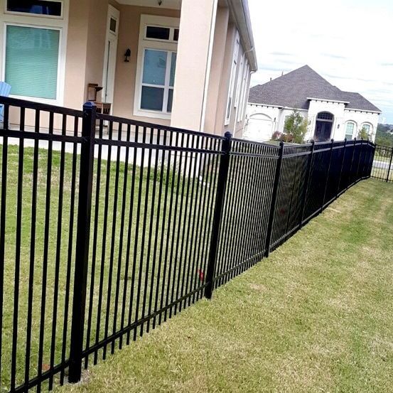 Black metal fence bordering a grassy yard with a house in the background.