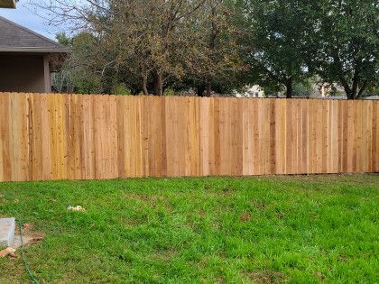Wooden fence in a backyard with green grass, trees, and a house in the background.