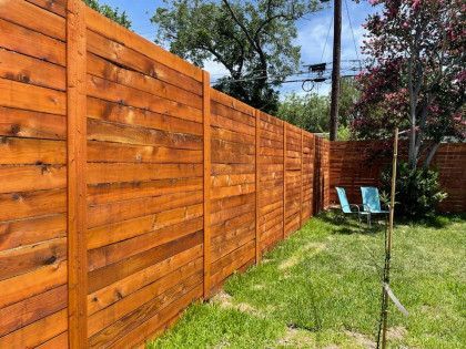Wooden fence in a backyard with two chairs, grass, and a tree.