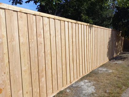 Wooden fence in a yard, made of vertical planks.
