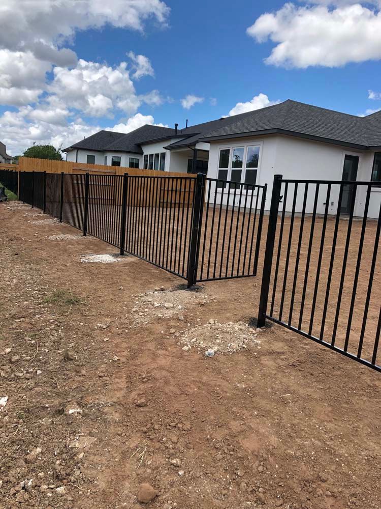Black metal fence with matching gate in front of light-colored house under a partly cloudy sky.