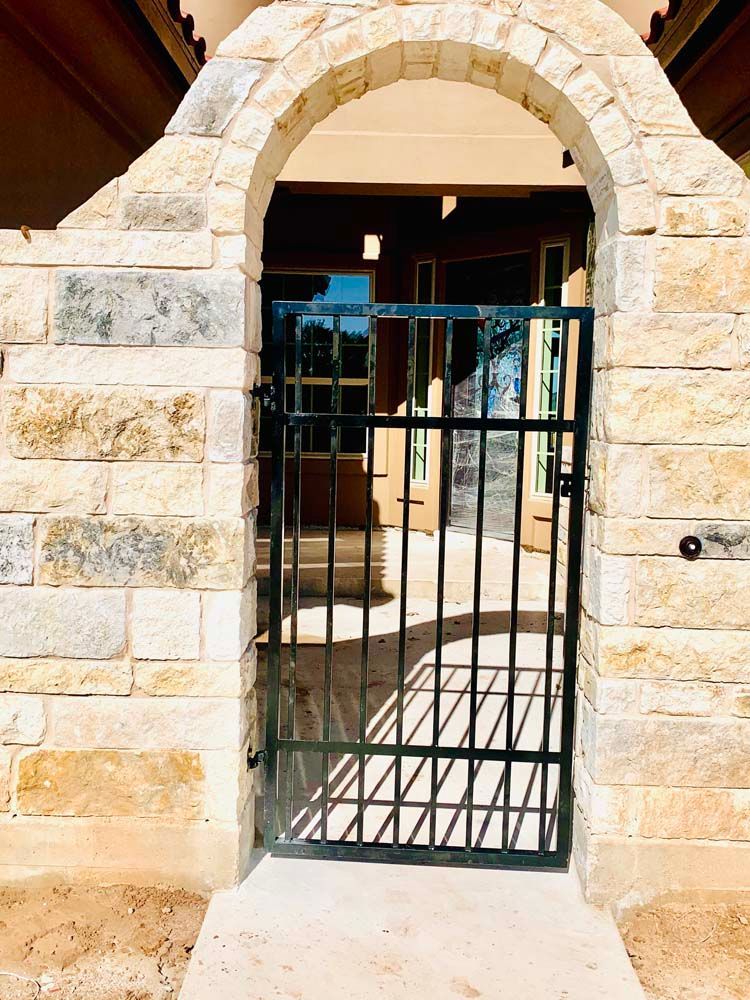 Black metal gate set in a sandstone archway, opening to a porch.